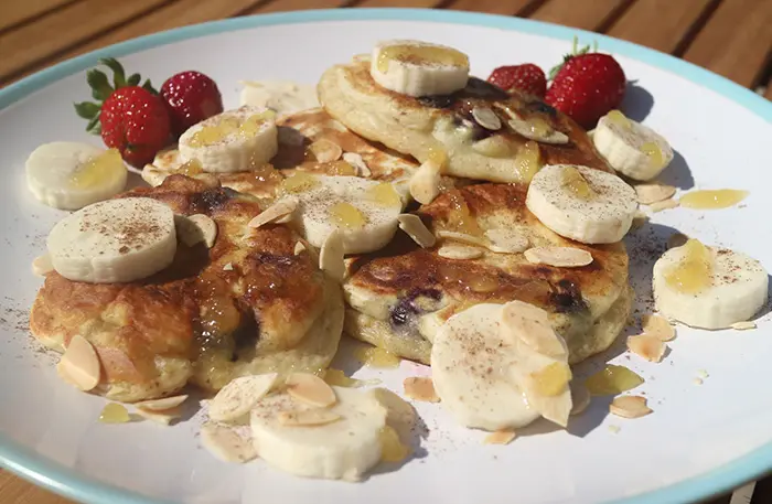 A large stack of banana, blueberry and lemon pancakes on a plate with fresh strawberries in the background.
