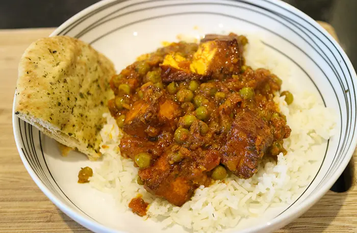 The finished Mattar paneer curry, served in a white bowl with some Naan bread on the side. 