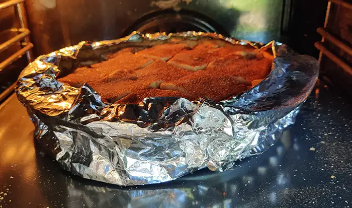 The pie baking in the oven. The edge of the pie is wrapped with a collar of silver foil to protect it from being overcooked
