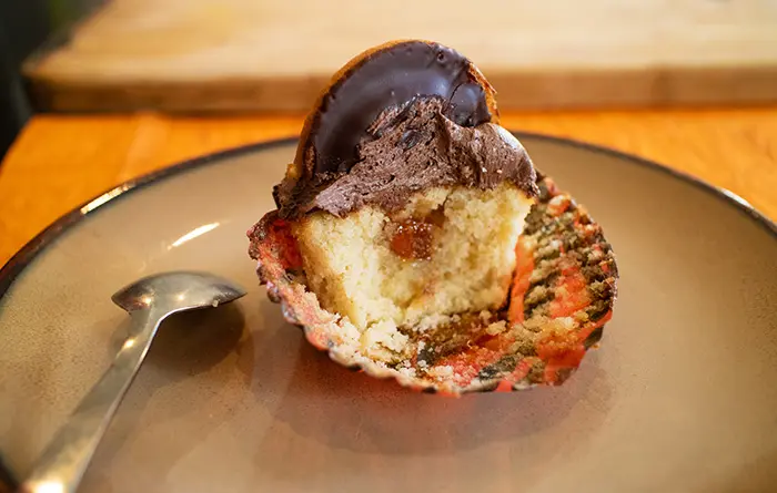 A Jaffa cake cupcake that's half eaten, showing the orange marmalade filling inside it