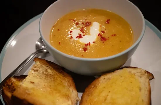 Butternut squash soup with chilli & crème fraîche in a blue bowl and some crusty buttered bread on the side